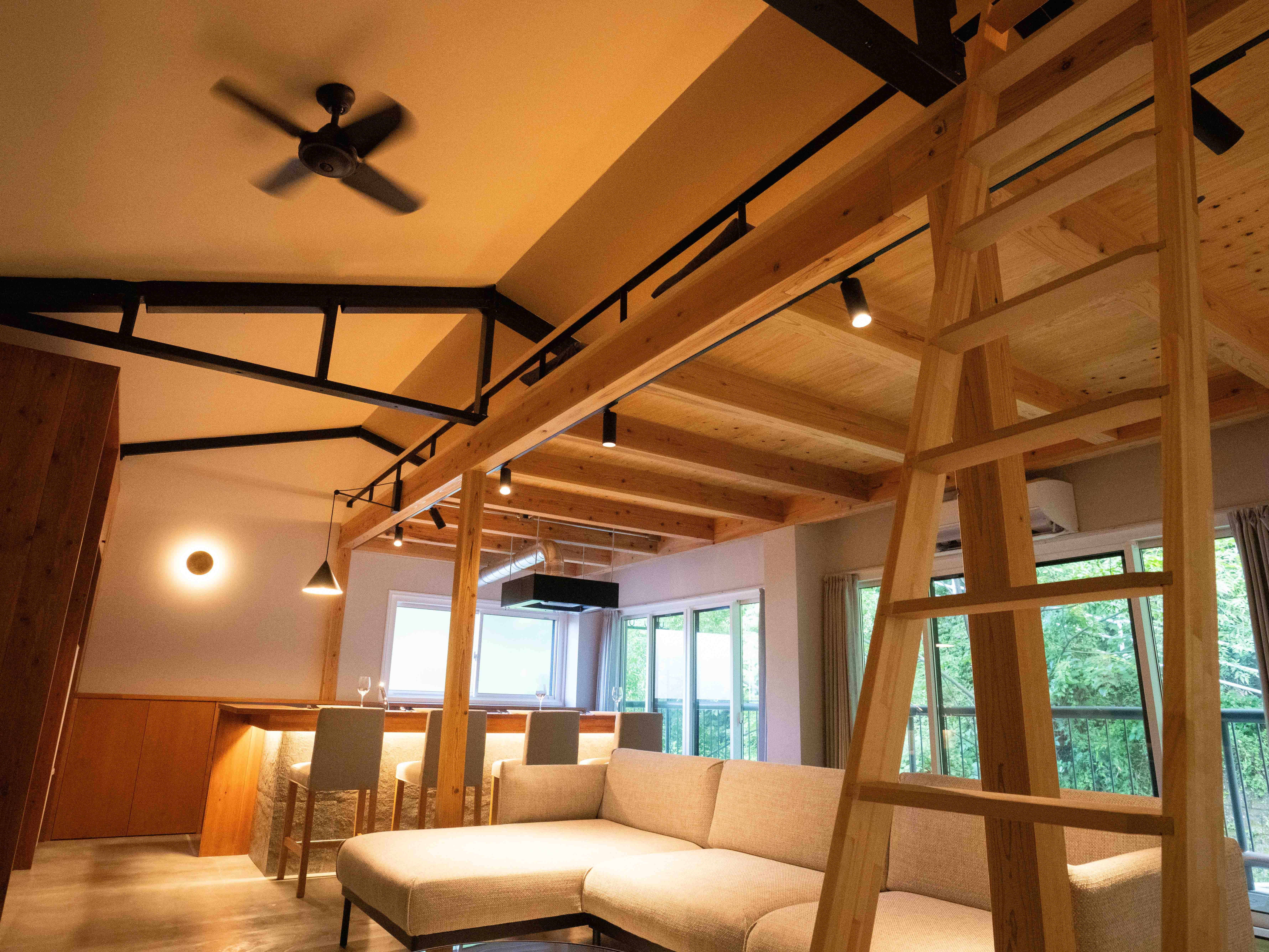 空き家をリノベーションした一棟貸しの宿のリビング。梁を活かした吹き抜けと窓の外の緑(Hotel Re:Plug)